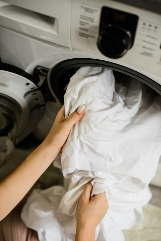 Person loading a white sheet into a front-loading washing machine using a gentle grip on the fabric.
